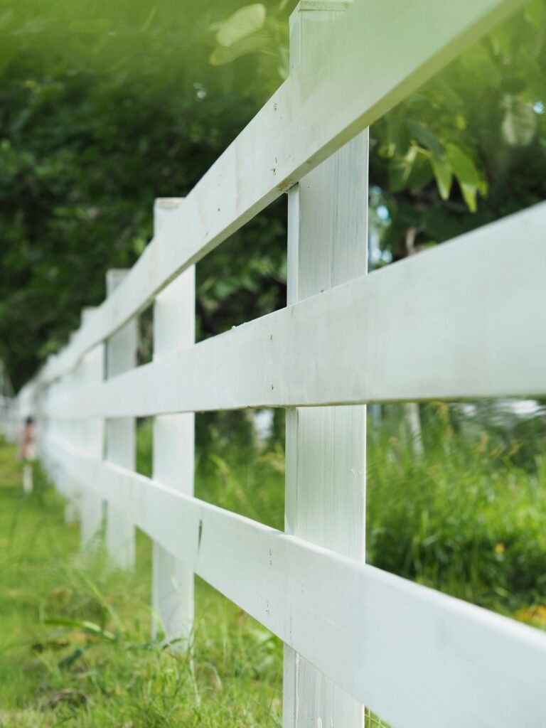 Close-up of a white wooden fence in a lush green field during a clear day.